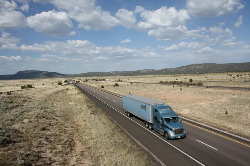 Tractor-trailer heading along Interstate 40 through the high desert of Arizona under a cloudy sky