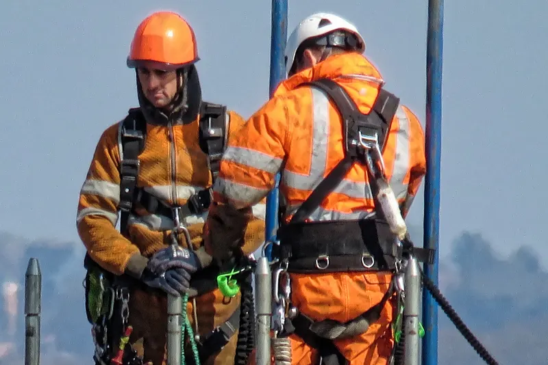 Two construction workers in hard hats, high-visibility clothing and safety harnesses on a building site in London