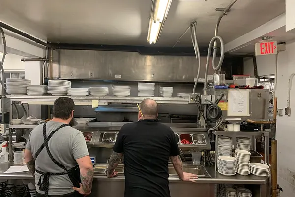 Restaurant kitchen expo station with stacked plates and two cooks at the pass