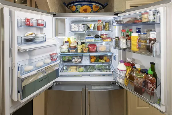Open refrigerator with covered containers, produce, eggs and packaged food on separate shelves