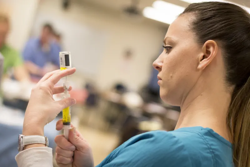 Nursing student preparing a syringe during practice in a college nursing skills lab