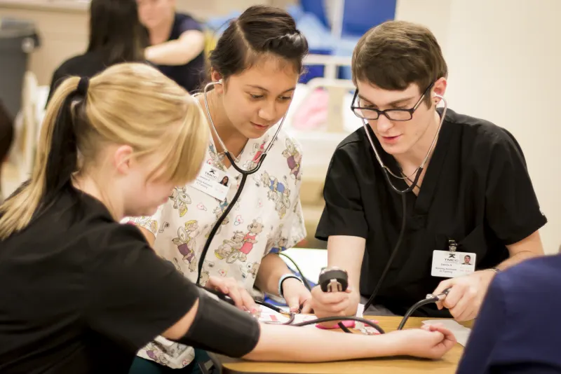 Nursing assistant students practicing blood pressure checks with stethoscopes in a training lab