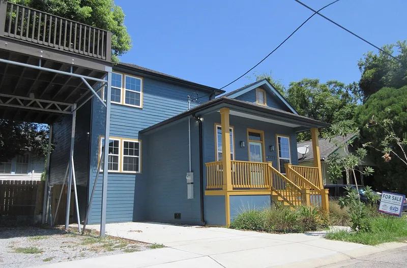 Newly built blue two-story house with a yellow porch and a For Sale sign in the front yard