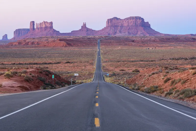 Straight two-lane highway leading toward the buttes of Monument Valley at dawn, U.S. Route 163