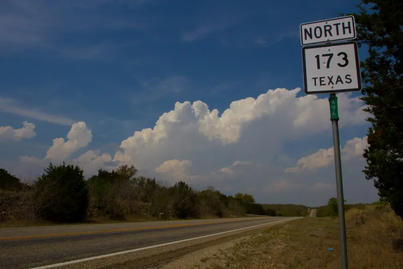 Texas state highway sign beside a rural two-lane road under a big sky in Medina County, Texas